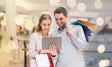 casal usando aplicativo de vendas em tablet segurando sacvolas de compras