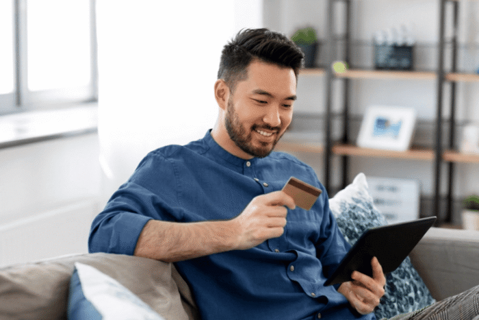 homem utilizando tablet e segurando cartão de crédito, representando comportamento de consumo digital e decisão de compra.