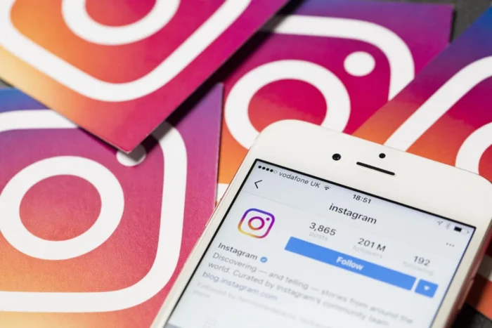 smartphone com aplicativo instagram em tela e logo de instagram ao fundo