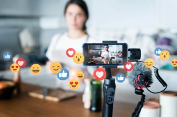digital influencer criando conteudo de vlog com o tema de culinaria em smartphone com simbolos de reaçoes do aplicativo facebook em sua volta