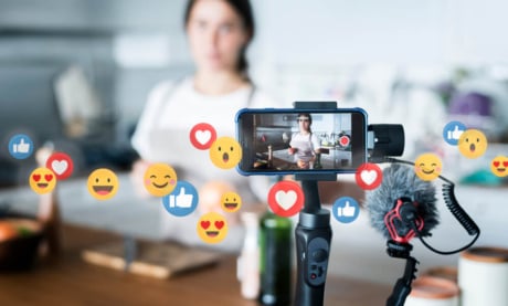 digital influencer criando conteudo de vlog com o tema de culinaria em smartphone com simbolos de reaçoes do aplicativo facebook em sua volta