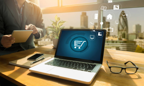 laptop em mesa de escritorio com simbolo de carrinho de compras em tela simbolizando o e- commerce