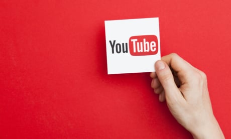 mao segurando nota com icone da plataforma youtube em fundo vermelho