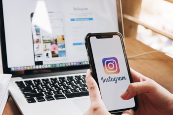 maos femininas segurando smartphone com logo de aplicativo instagram em tela em frente a laptop