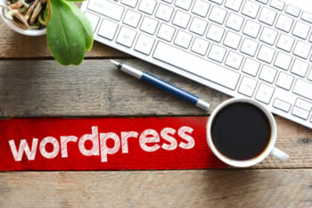 mesa de escritorio com teclado de computador, xicara de cafe e caneta com a palavra wordpress ao lado
