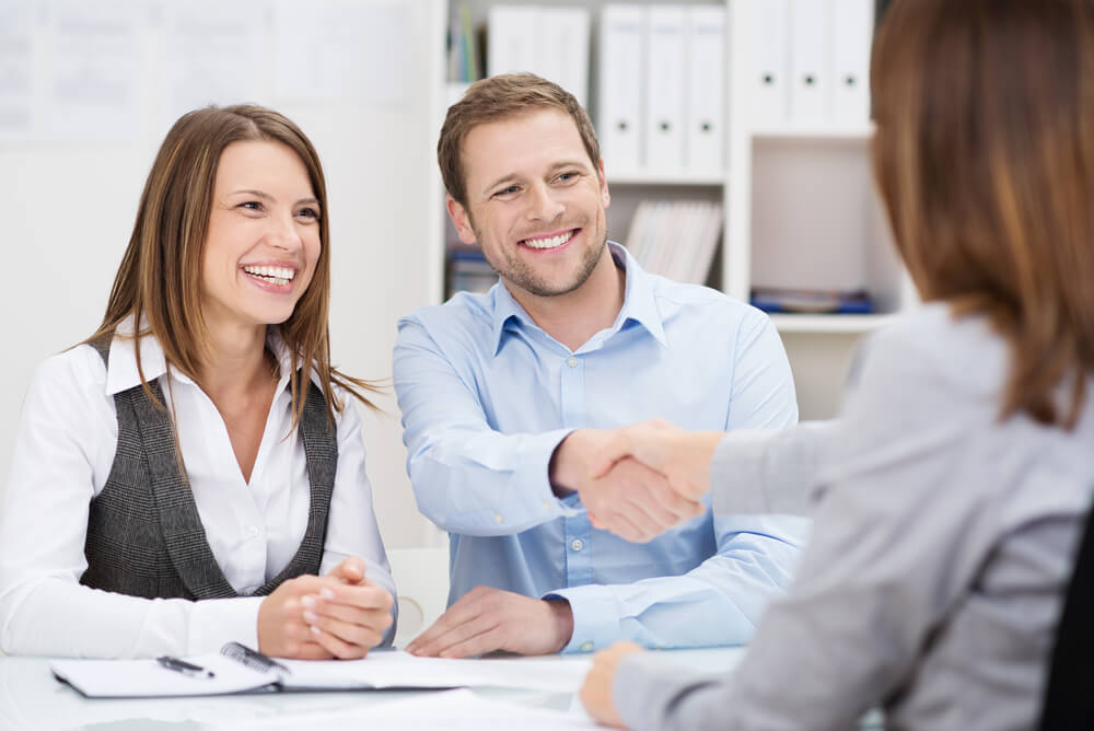 profissional apertando mao de clientes com expressao sorridente em escritorio simbolizando a satisfaçao do cliente