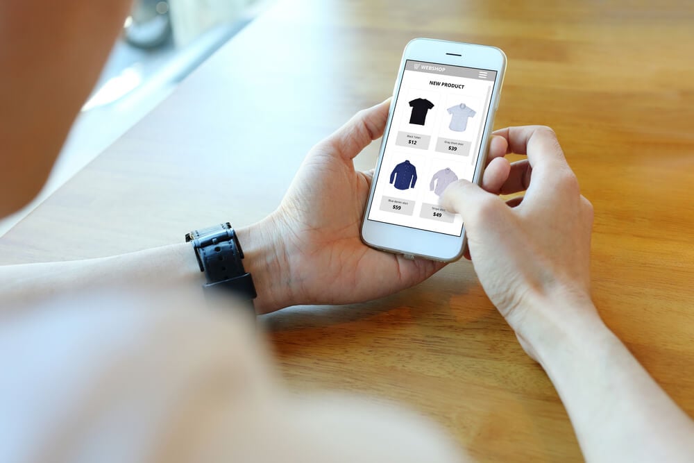 maos masculinas segurando smartphone com pagina de ecommerce em tela visualizando produtos