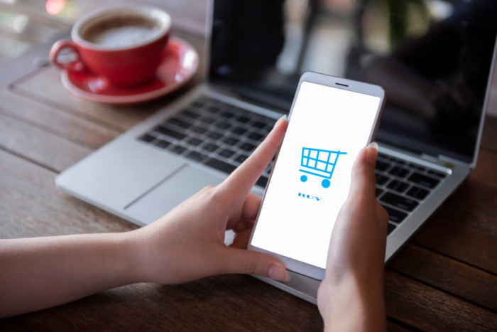 maos femininas segurando smartphone com carrinho de compras em tela simbolizando o e-commerce