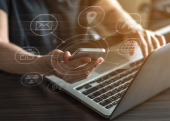 mãos masculinas segurando smartphone enquanto tecla em laptop com simbolos de SEO em destaque