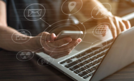 mãos masculinas segurando smartphone enquanto tecla em laptop com simbolos de SEO em destaque