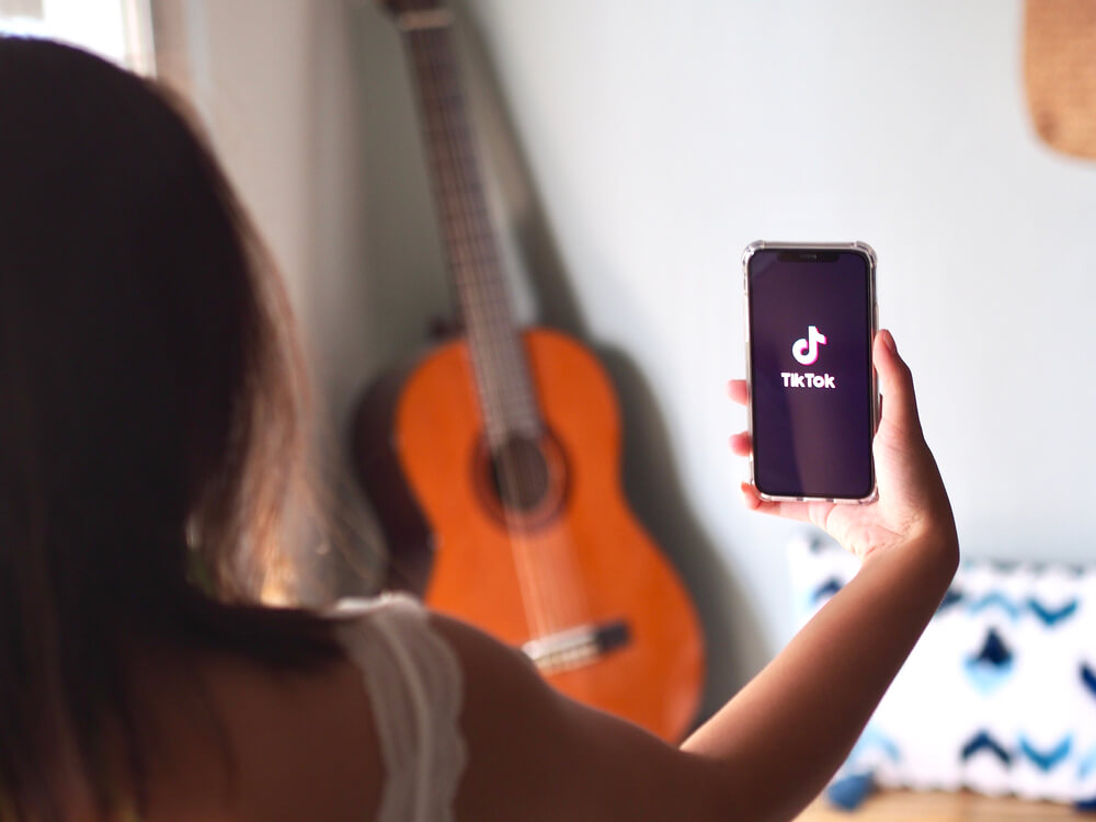 Mulher de costas com a tela do celular a mostra na tela do aplicativo Tik tok