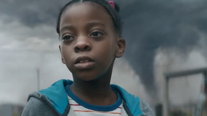 A little girl standing outside with a tornado in the background.