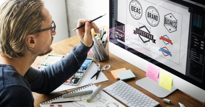 profissional em design em frente a computador escolhendo simbolo de logo de marca em mesa com materiais de escritorio