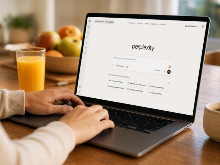 Pessoa usando notebook com tela na página inicial do Perplexity AI em ambiente claro, em cima de uma mesa de madeira com fruteira e copo de suco ao lado do notebook.