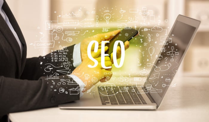 Símbolo do SEO com vários ícones associados sobreposto a pessoa acessando celular e notebook.