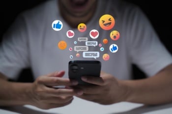 Pessoa acessando redes sociais com ícones de emojis surgindo na tela