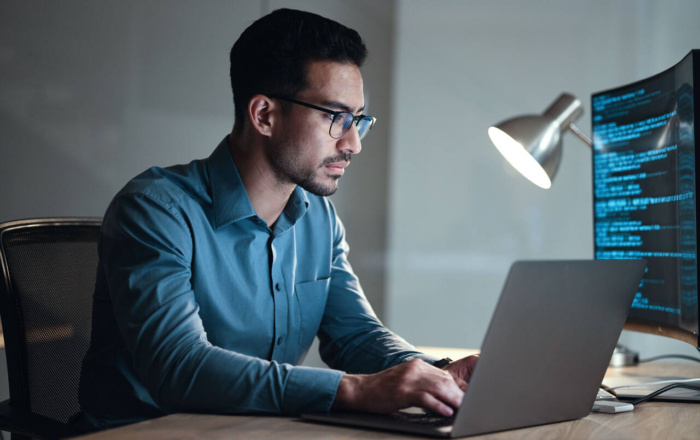 Programmatore al lavoro su laptop in ufficio, scrive codice e gestisce implementazioni digitali.