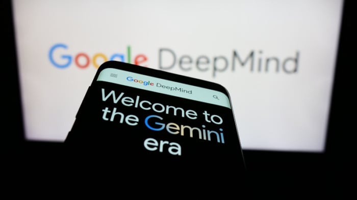 um celular com a palavras escritas welcome to the gemini era e um nootbok de fundo aberto no google deepmind