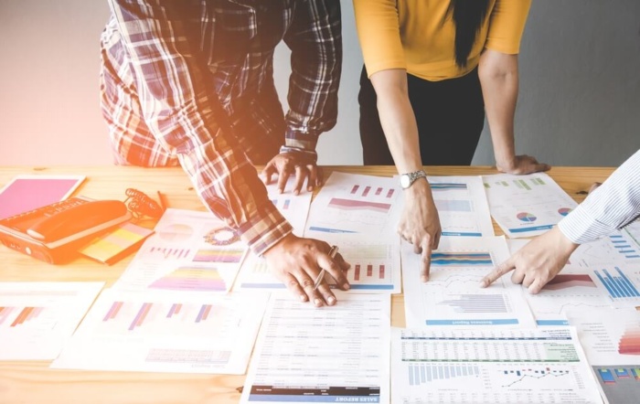 Grupo de profissionais analisando relatórios e gráficos de desempenho sobre a mesa, em um exemplo de como fazer um briefing para diferentes tipos de projetos de marketing.