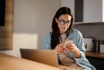 Mulher usando o celular e o notebook em casa para pesquisar informações e comparar marcas no Google, ilustrando o conceito de share of search.