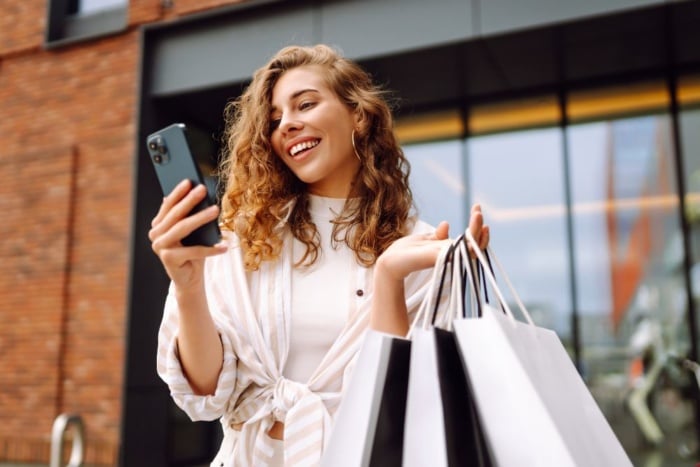 Mulher com sacolas de compras e olhando no celular produtos pelo Google Shopping