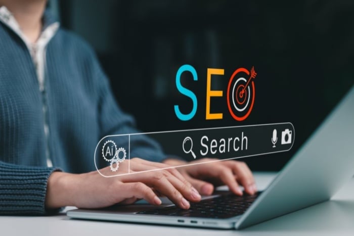 Pessoa digitando em um notebook com uma barra de pesquisa digital flutuante na tela contendo o termo SEO estilizado com um alvo, fazendo a pesquisa sobre métricas de AEO com SEO. 