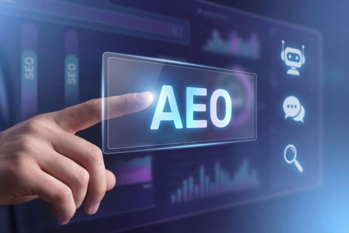Mão de um profissional apontando para uma tela digital com a sigla das métricas de AEO em destaque, ao lado de ícones de inteligência artificial, chatbot e motores de busca conversacional.