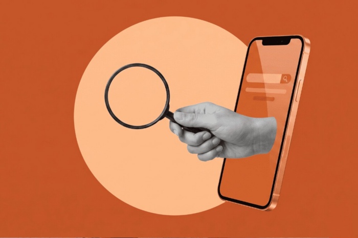 Ilustração em fundo laranja mostra uma mão segurando uma lupa diante de um smartphone com barra de busca na tela. A imagem representa pesquisa mobile e descoberta digital.